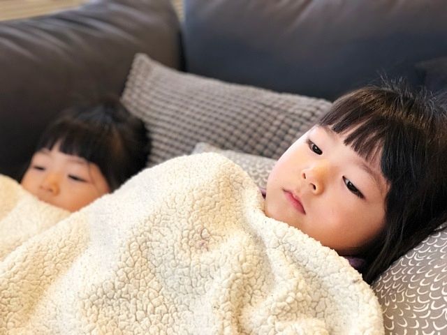 インフルエンザに感染し、毛布を掛けてソファーで休む姉妹