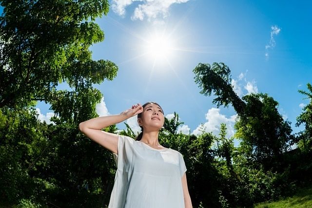 真夏の日差しの中で額の汗を拭く女性